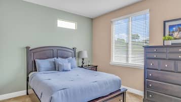 Une chambre à coucher comprenant un lit, une table de chevet, une commode et une fenêtre avec des stores.