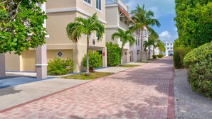A paved walkway lined with palm trees and greenery, leading to a building with a beige facade and multiple windows.