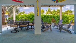 An outdoor covered patio with a table and chairs, surrounded by lush greenery and palm trees. - Oceanview Rooftop Retreat  3BR 3BA in Marathon FL (Marathon)