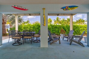 An outdoor covered patio with a table and chairs, surrounded by lush greenery and palm trees. - Oceanview Rooftop Retreat  3BR 3BA in Marathon FL (Marathon)