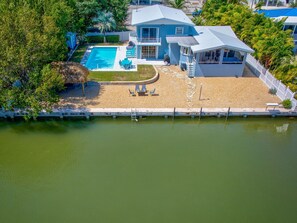 A two-story house with a swimming pool, a covered patio, and a dock extending into a body of water.