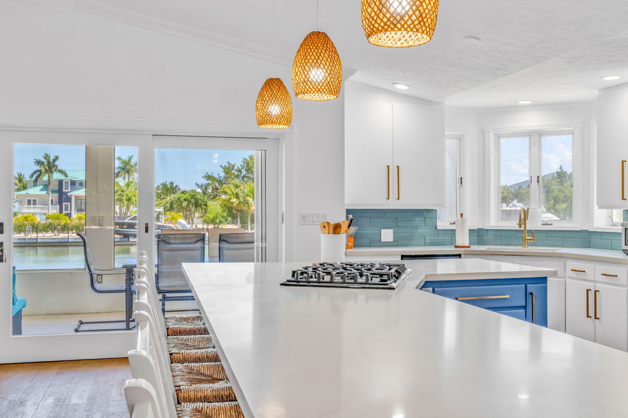 A modern kitchen with a large island, white cabinetry, and a view of a pool and palm trees.