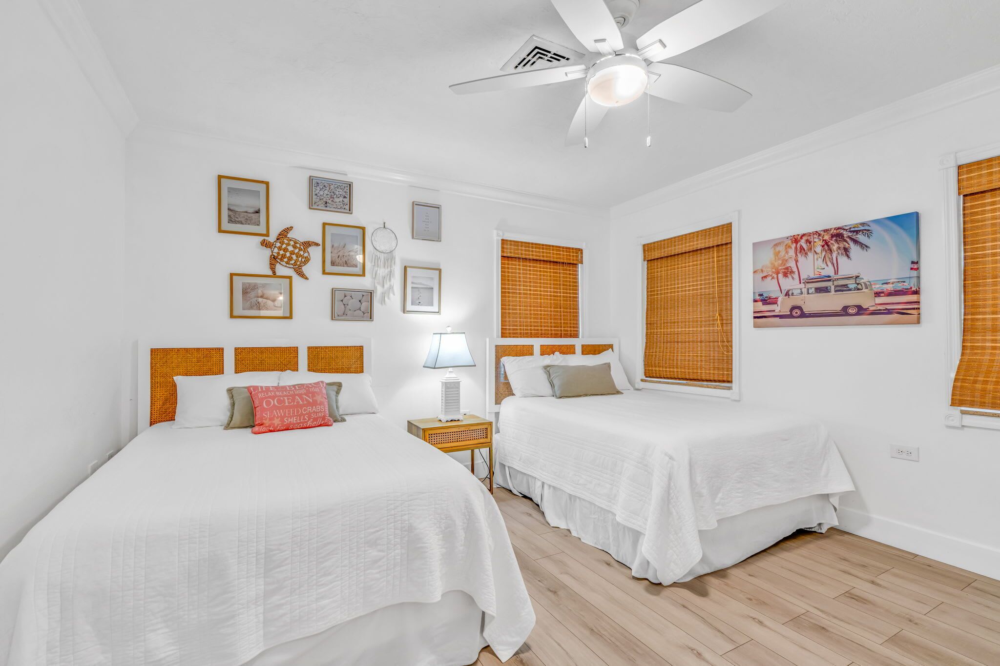 A room with two beds, a ceiling fan, and framed pictures on the wall.