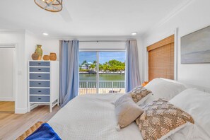 Une chambre avec un grand lit, une commode et une vue sur un plan d’eau, accessible par une porte coulissante.