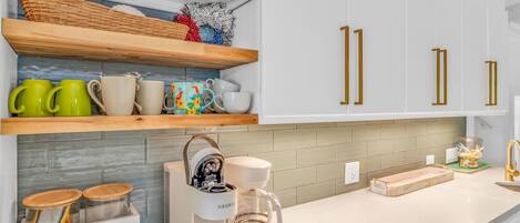 A modern kitchen with white cabinets, a coffee bar, and a coffee maker.
