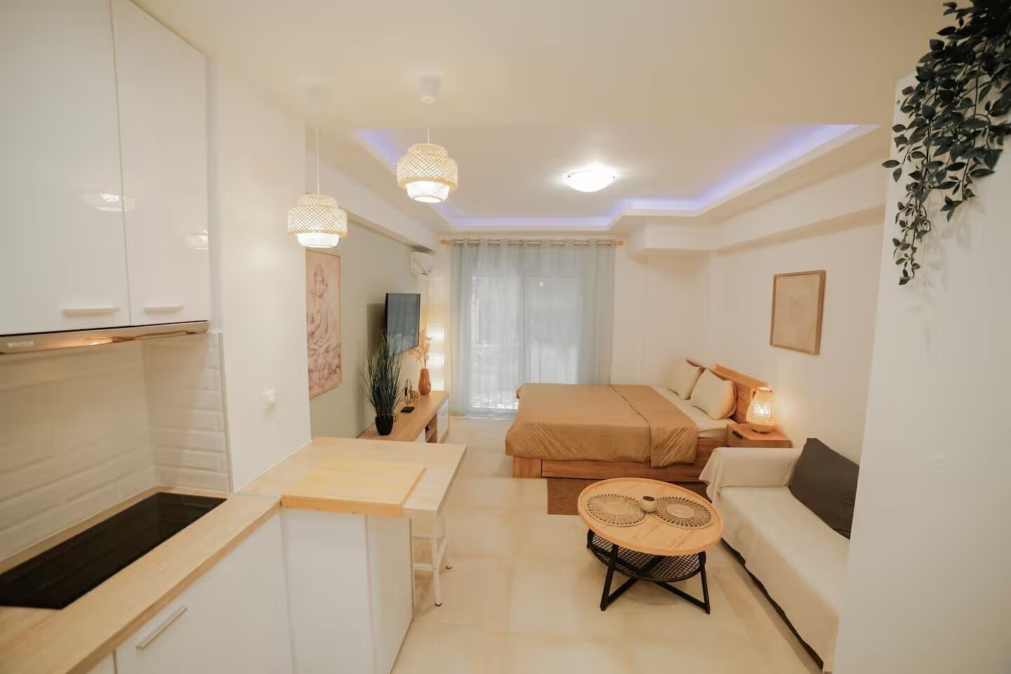 A compact hotel room with a kitchenette, a bed, a small round table, and a TV.