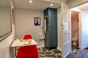 A room with a dining table, red chairs, a cabinet, a framed notice, and a bathroom visible through an open door.