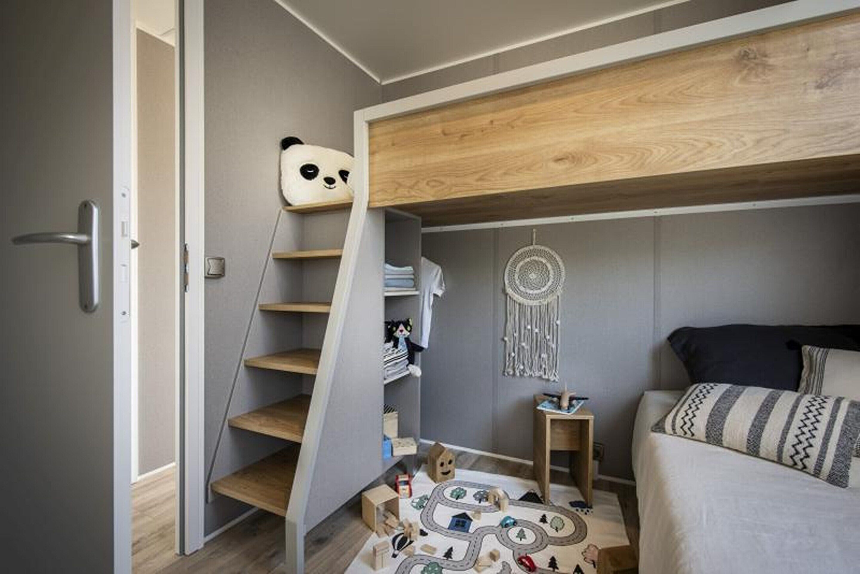A bedroom with a bunk bed, a wooden staircase, a dreamcatcher, and a play area with toys.