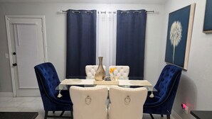 A dining area with a glass table, two blue velvet chairs, a white tufted chair, and a vase with flowers. - Yukon home (Yukon)