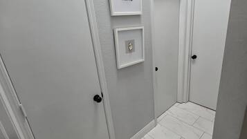 Un couloir avec des portes blanches, un sol en marbre et deux tableaux encadrés accrochés au mur.