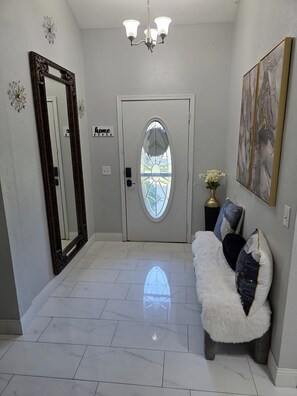 A hallway with a white door, a mirror, a chandelier, and a sofa with decorative pillows. - Yukon home (Yukon)