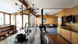 A rustic wooden interior with a long dining table, multiple light fixtures, and a television on the wall.