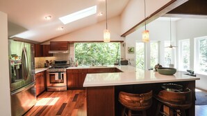 A modern kitchen with a large island, wooden cabinets, and a view of greenery outside.