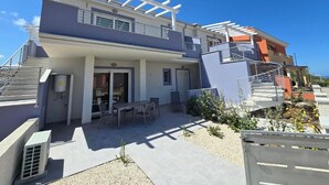 A modern two-story house with a patio area, outdoor seating, and a covered staircase. - Home Geranio With Private Garden (Castelsardo)