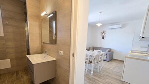 A modern bathroom with a sink and mirror, a shower area, and a dining area with a table and chairs. - Home Geranio With Private Garden (Castelsardo)