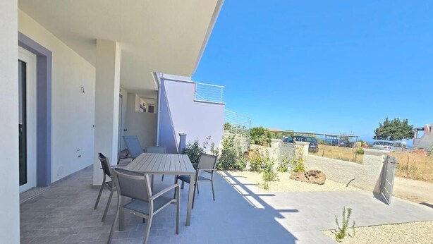 An outdoor patio with a table and chairs, a small garden area, and a view of the surrounding landscape. - Home Geranio With Private Garden (Castelsardo)
