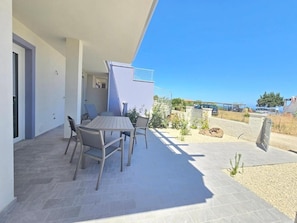 An outdoor patio with a table and chairs, a small garden area, and a view of the surrounding landscape. - Home Geranio With Private Garden (Castelsardo)