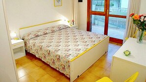 Ein Schlafzimmer mit Bett, Nachttisch, Lampe, einem Fenster mit Blick und einem kleinen Tisch mit einer Vase.
