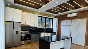 A modern kitchen with a central island, stainless steel appliances, and a wooden ceiling with linear lighting.