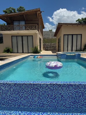 Una piscina con mosaicos azules, un flotador y vistas a dos edificios con balcones y cortinas.