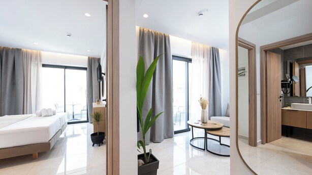 Habitación de hotel moderna con cama, una mesita, una planta en maceta y un baño con espejo y lavabo.