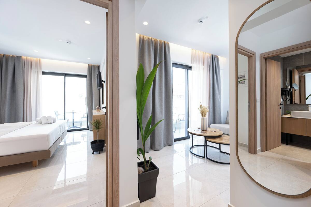 Habitación de hotel moderna con cama, una mesita, una planta en maceta y un baño con espejo y lavabo.