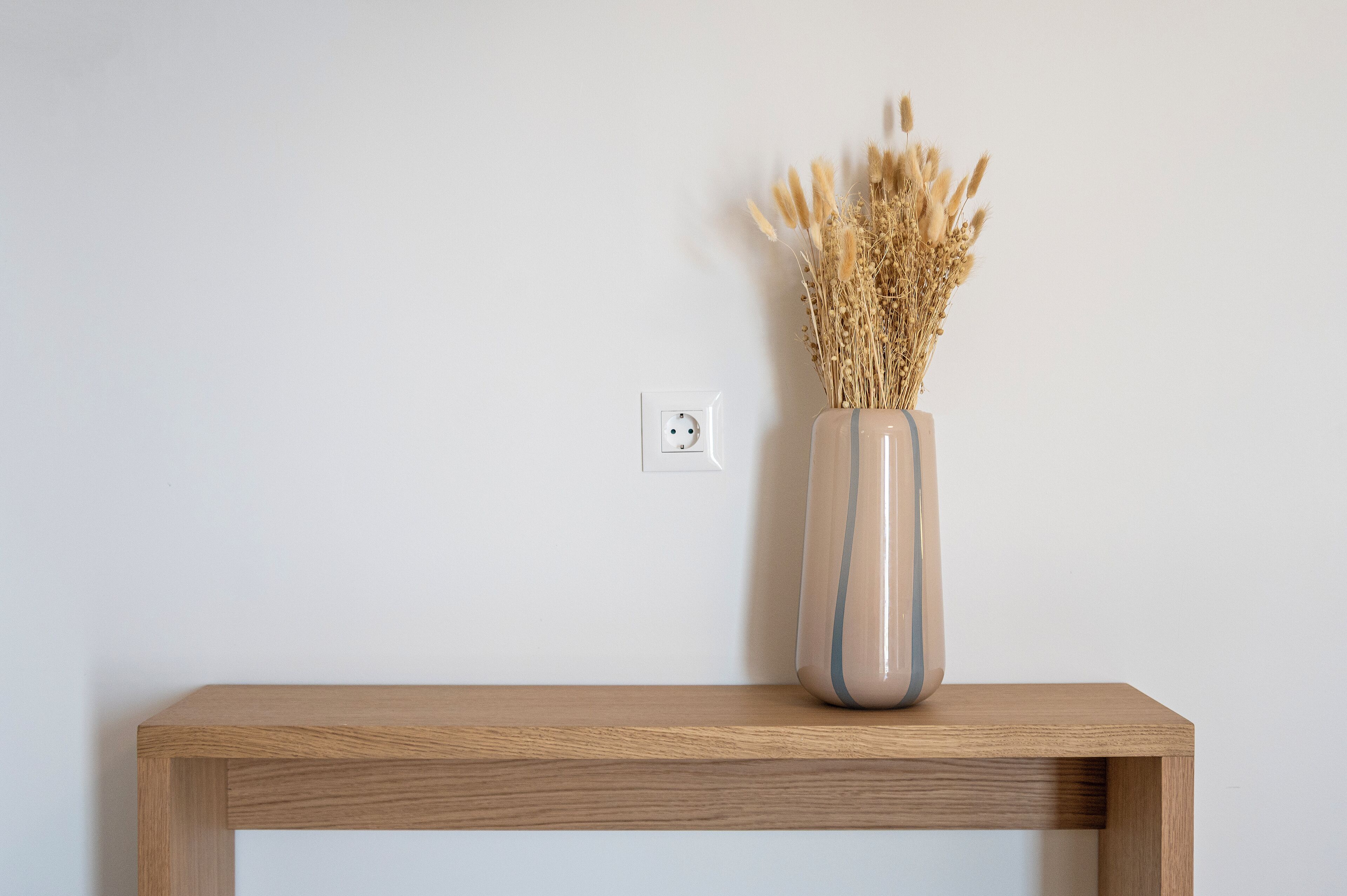 Ein Holztisch mit einer Vase getrockneter Pflanzen vor einer schlichten Wand.