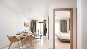 Una habitación de hotel moderna con cama, zona de comedor con mesa y sillas, y un ventanal con cortinas.