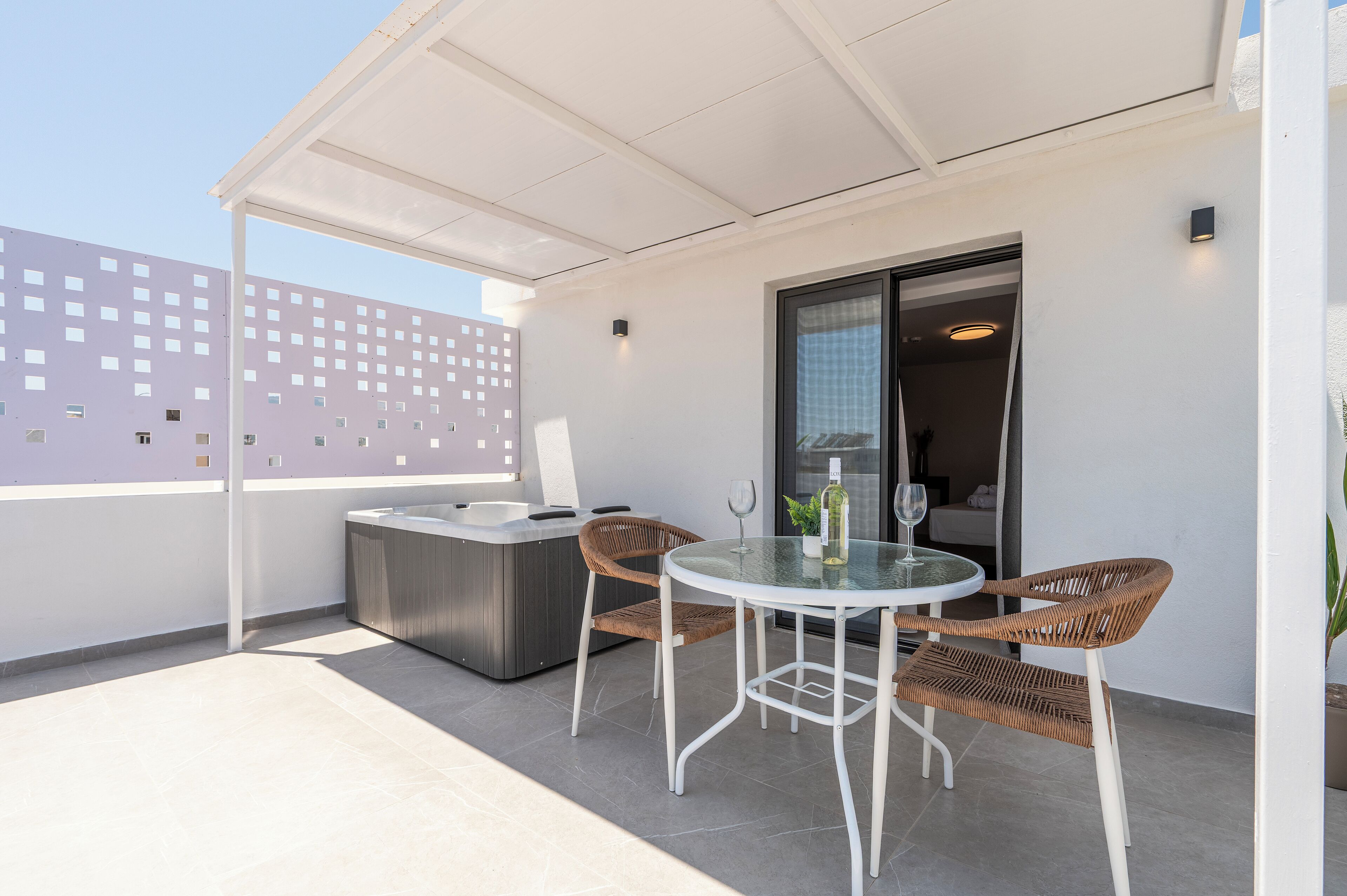 Un patio exterior moderno con una mesa de vidrio, sillas de mimbre, un jacuzzi y vistas a un edificio con fachada ornamentada.
