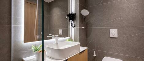 A modern bathroom with a large mirror, a white sink, a hairdryer, and a toilet.
