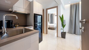 Una cocina moderna con un lavamanos de acero inoxidable, un horno empotrado y una cafetera. Hay una planta en maceta en el pasillo y una cama con cortina gris en la habitación contigua.