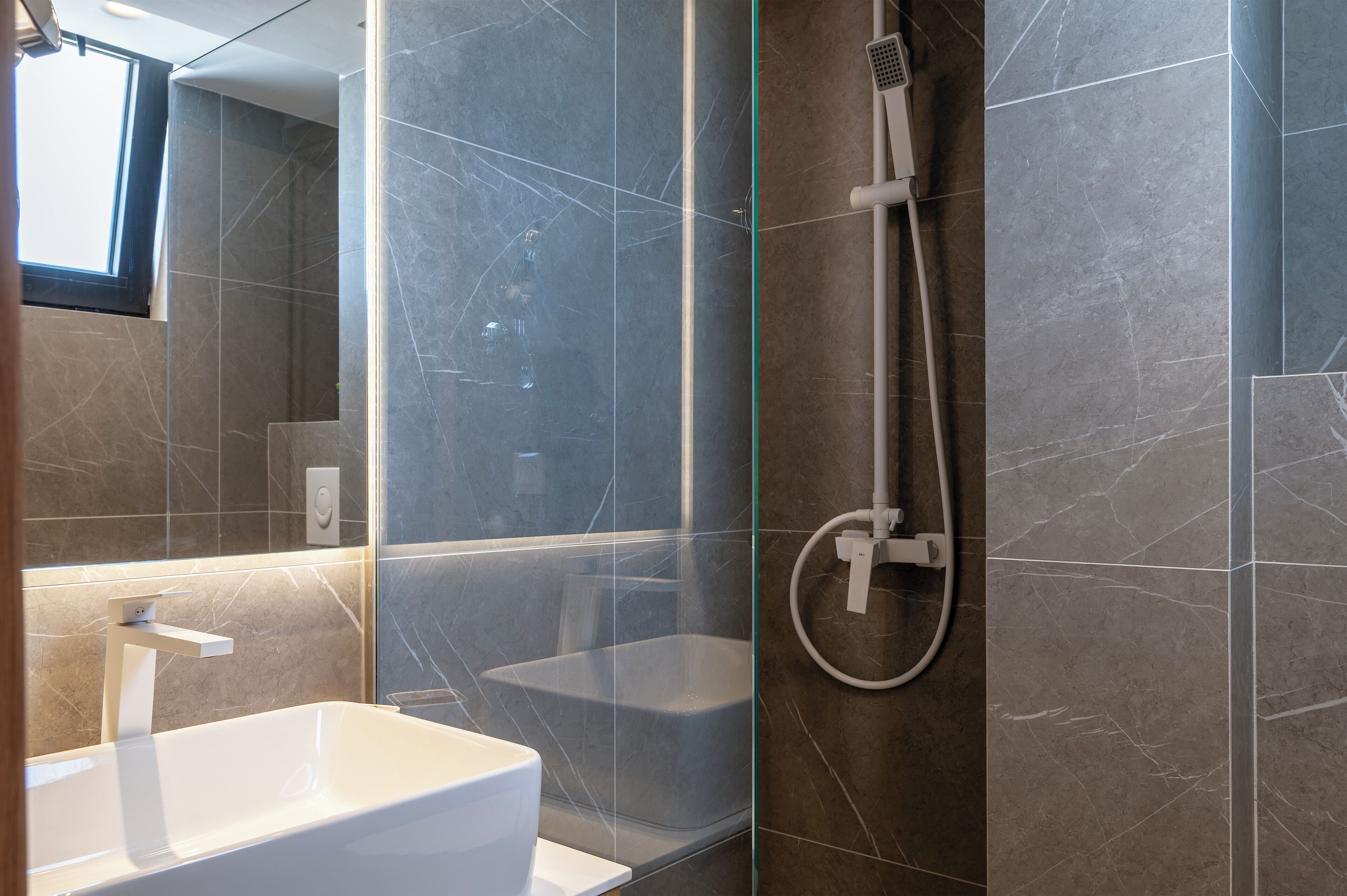 Ein modernes Badezimmer mit einer gläsernen Duschkabine, einem weißen Waschbecken und Marmorfliesen.