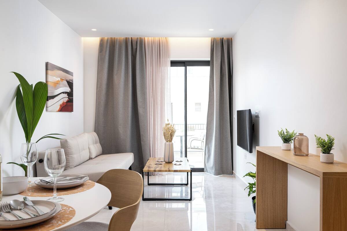 Una sala de estar moderna con comedor, un sofá, una mesa de centro y un televisor montado en la pared.