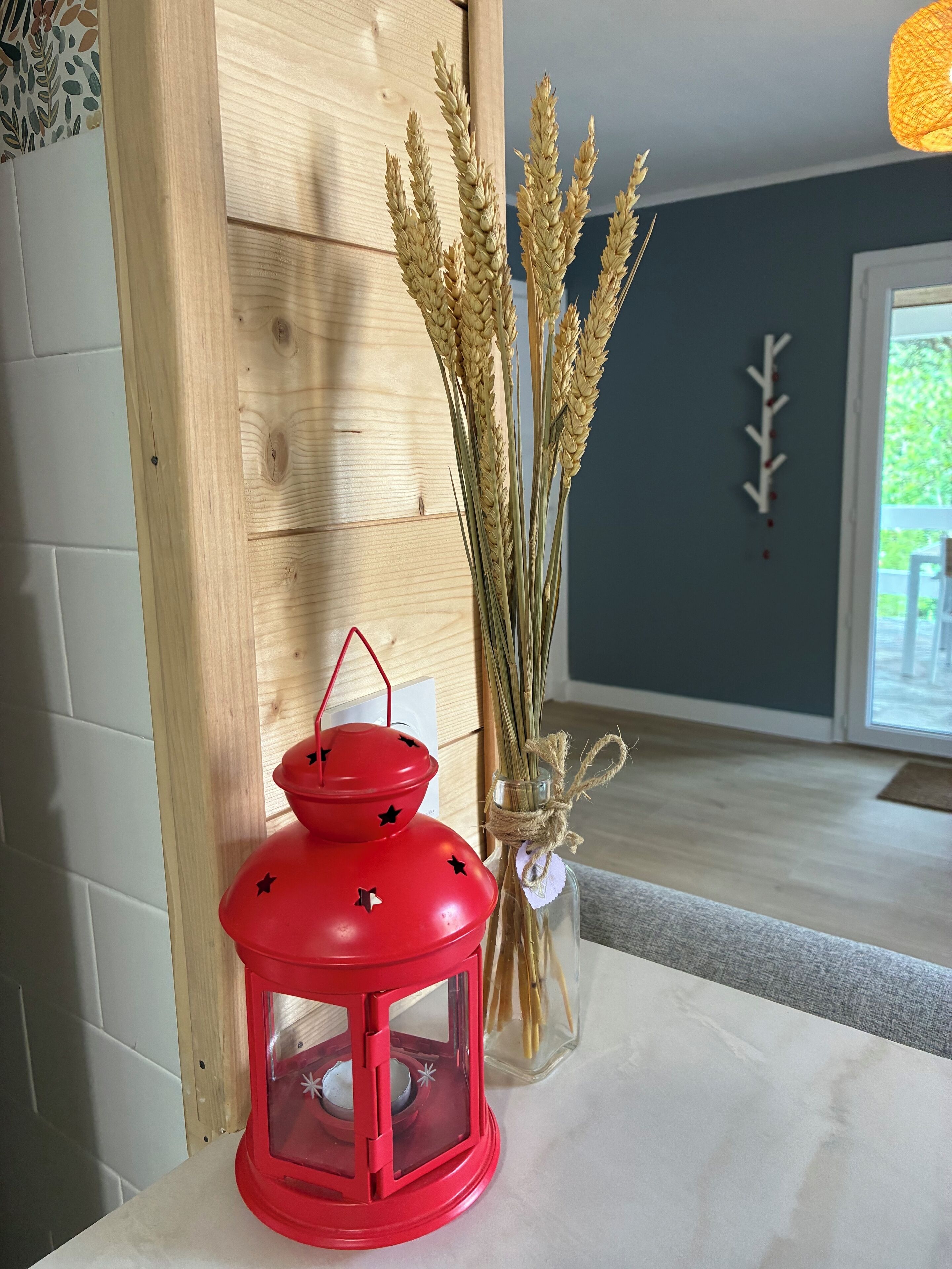 A red lantern with black stars, a vase with dried wheat stalks, and a wooden wall.