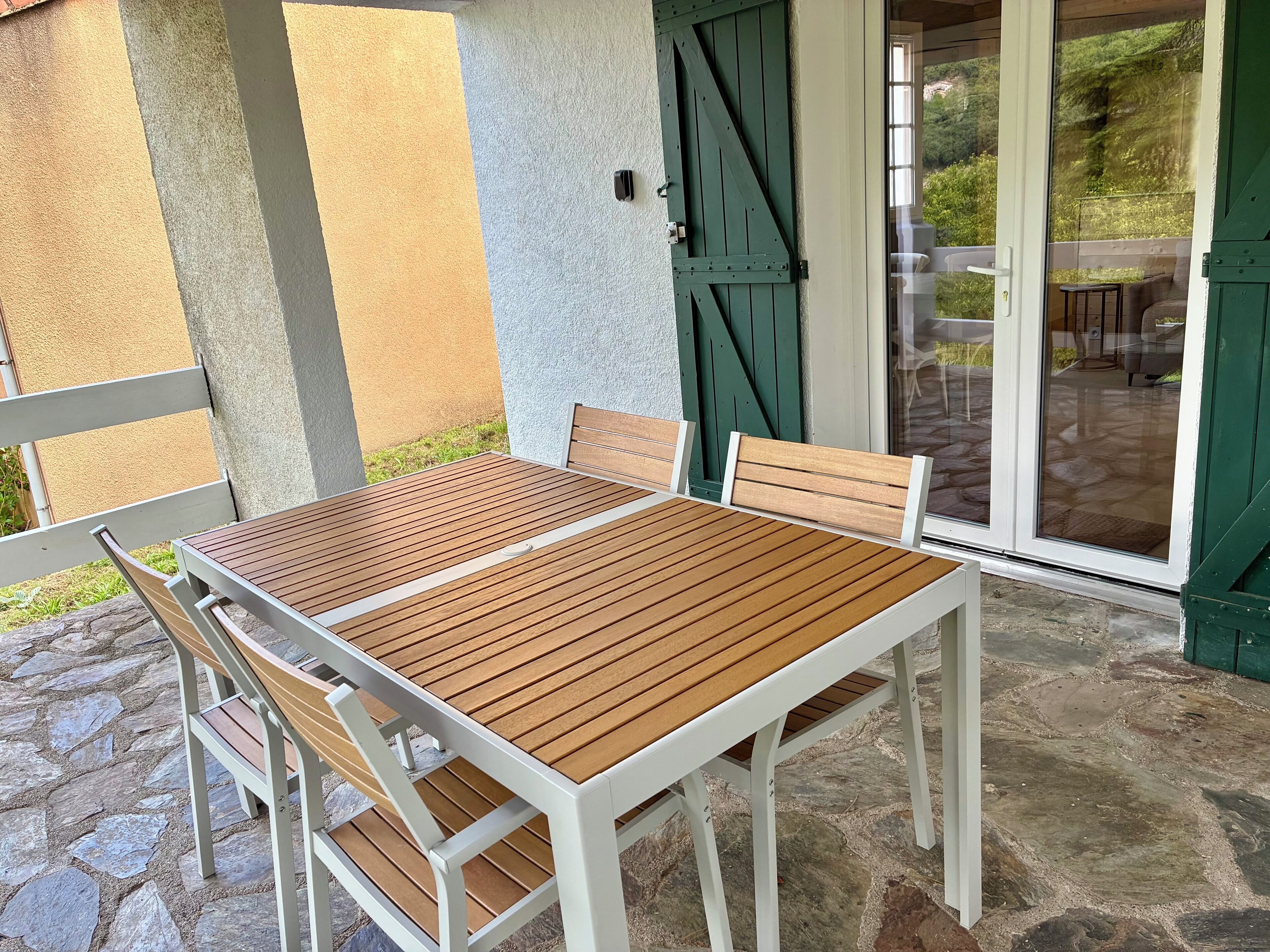 A patio with a wooden table and chairs, a stone floor, and a green door.