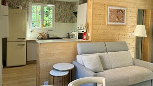 Ein gemütliches Wohnzimmer mit grauem Sofa und kleinem weißen Sessel, eine Holz-Küche mit Fenster und einem gerahmten Bild an der Wand.