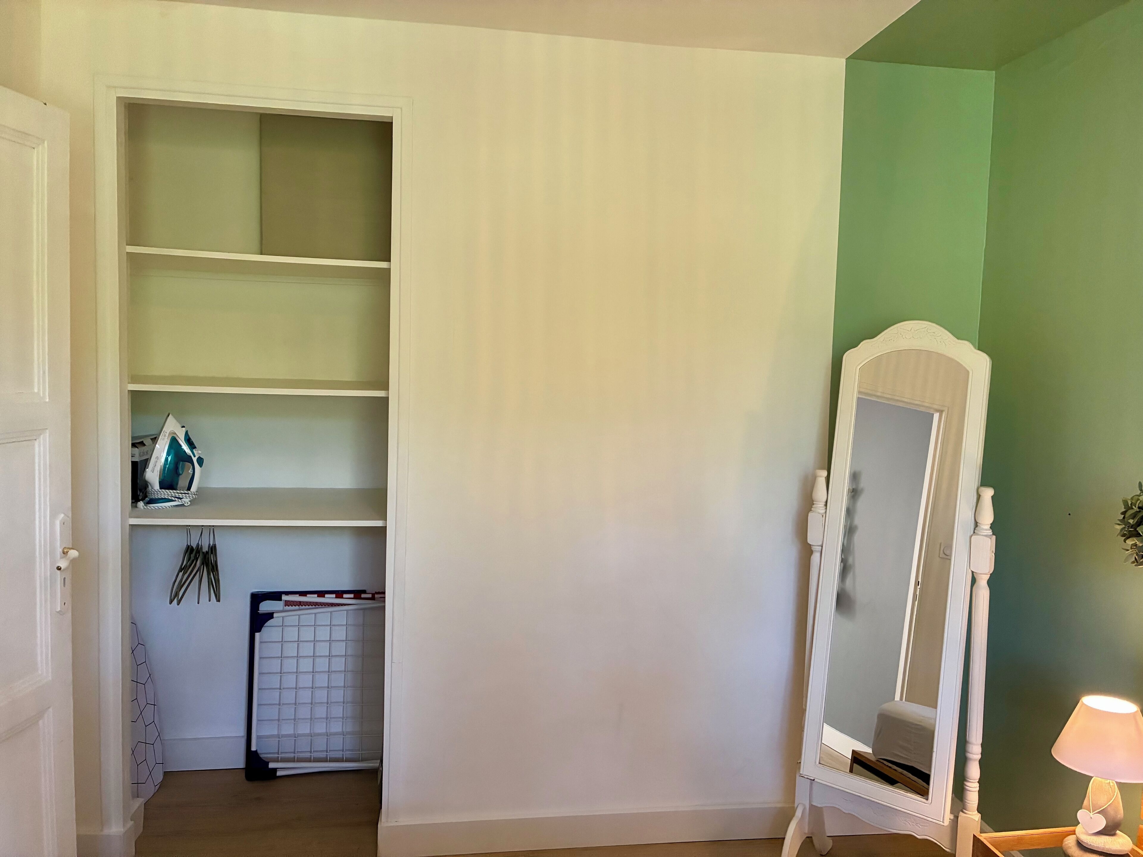 Una habitación con un armario blanco, un espejo y una lámpara.