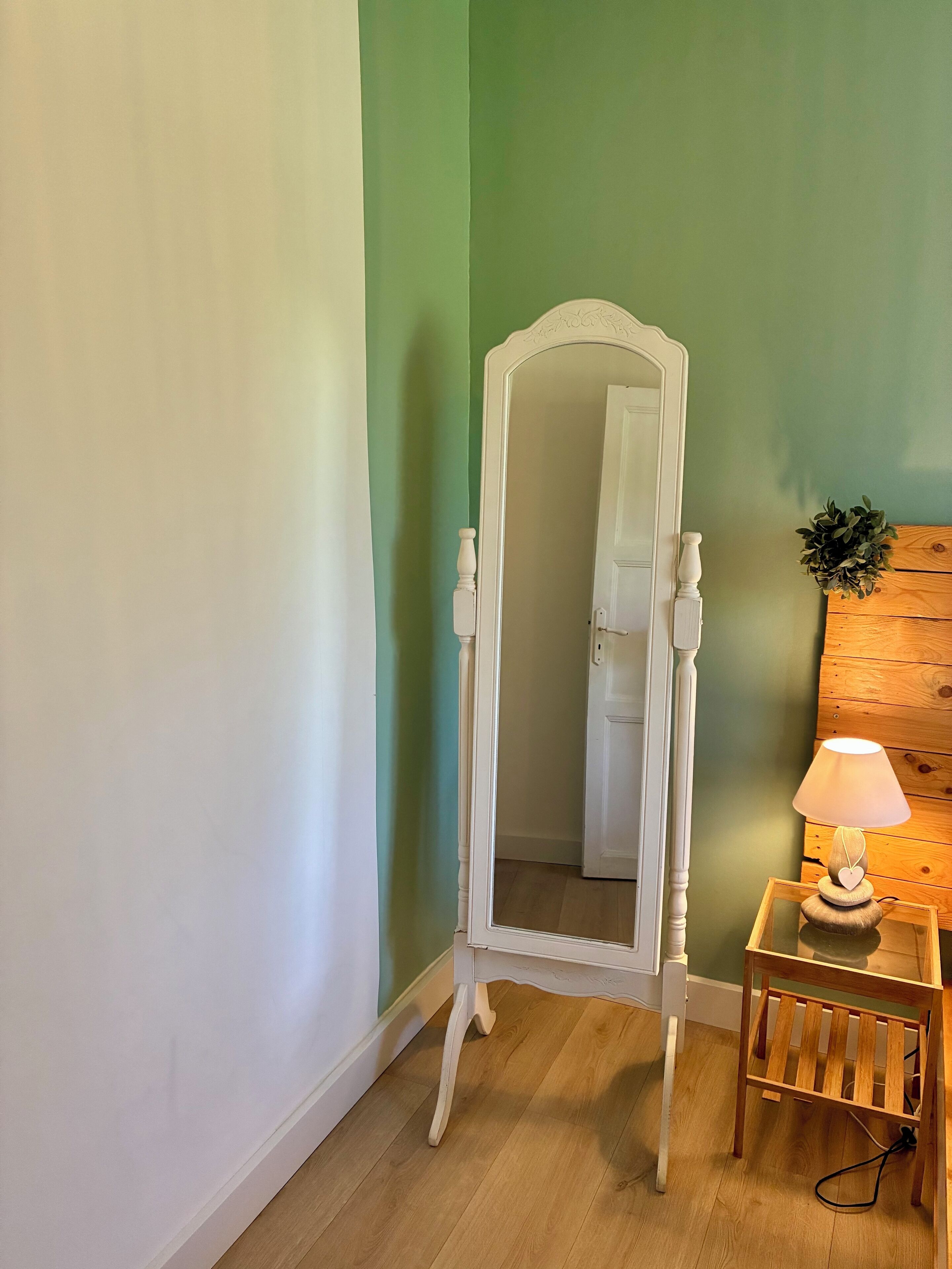 Ett rum med en vit sminkbord, ett träbord med en lampa och en spegel som reflekterar en dörr.