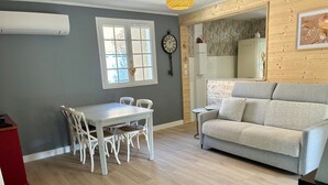 Ein modernes Wohnzimmer mit einem grauen Sofa, einem weißen Esstisch mit Stühlen und einem kleinen Beistelltisch.