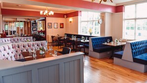 A restaurant with a bar area, seating arrangements, and a view of the city through large windows. - The Raven (Claines)
