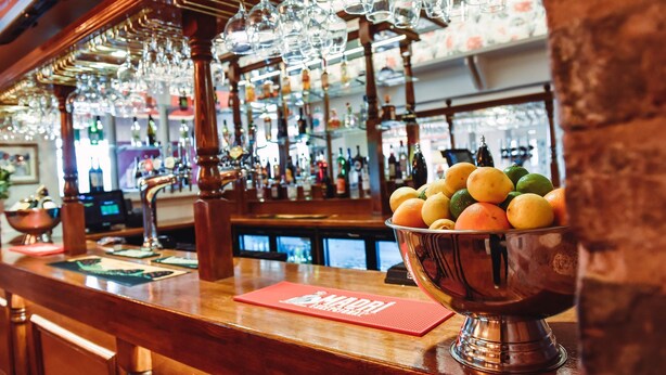 A bar area with a wooden counter, a bowl of fruit, and hanging glasses. - The Raven (Claines)