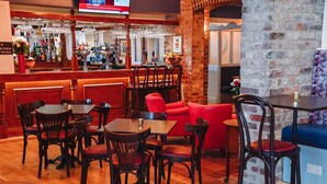 A bar area with wooden tables and chairs, a counter with a TV screen, and a brick wall. - The Raven (Claines)