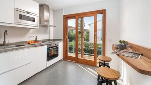 A modern kitchen with white cabinets, a stainless steel oven, and a wooden dining area with a table and stools.