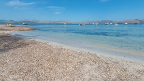 A beach with clear water, boats, and distant mountains.