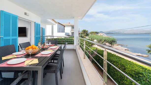 A balcony with a table set for dining, overlooking a body of water and greenery.