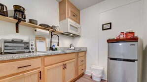 A compact kitchen with wooden cabinets, a stainless steel refrigerator, a built-in microwave, a toaster, and a coffee maker. - Cozy Urban Getaway Near Paseo Arts 31A (Oklahoma City)