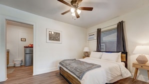 A bedroom with a wooden floor, a bed with white bedding, a ceiling fan, a bedside lamp, and a window with curtains. - Cozy Urban Getaway Near Paseo Arts 31A (Oklahoma City)