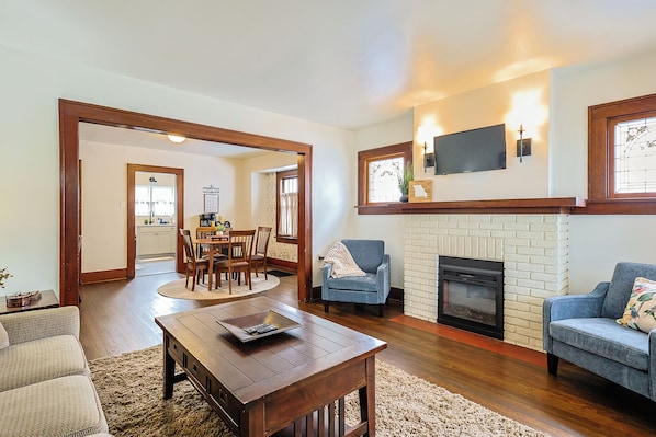 A living room with a fireplace, a dining area, and a kitchen in the background.
