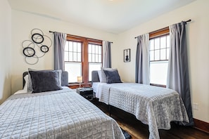 A hotel room with two beds, a wooden floor, a wall-mounted artwork, and a window with curtains.