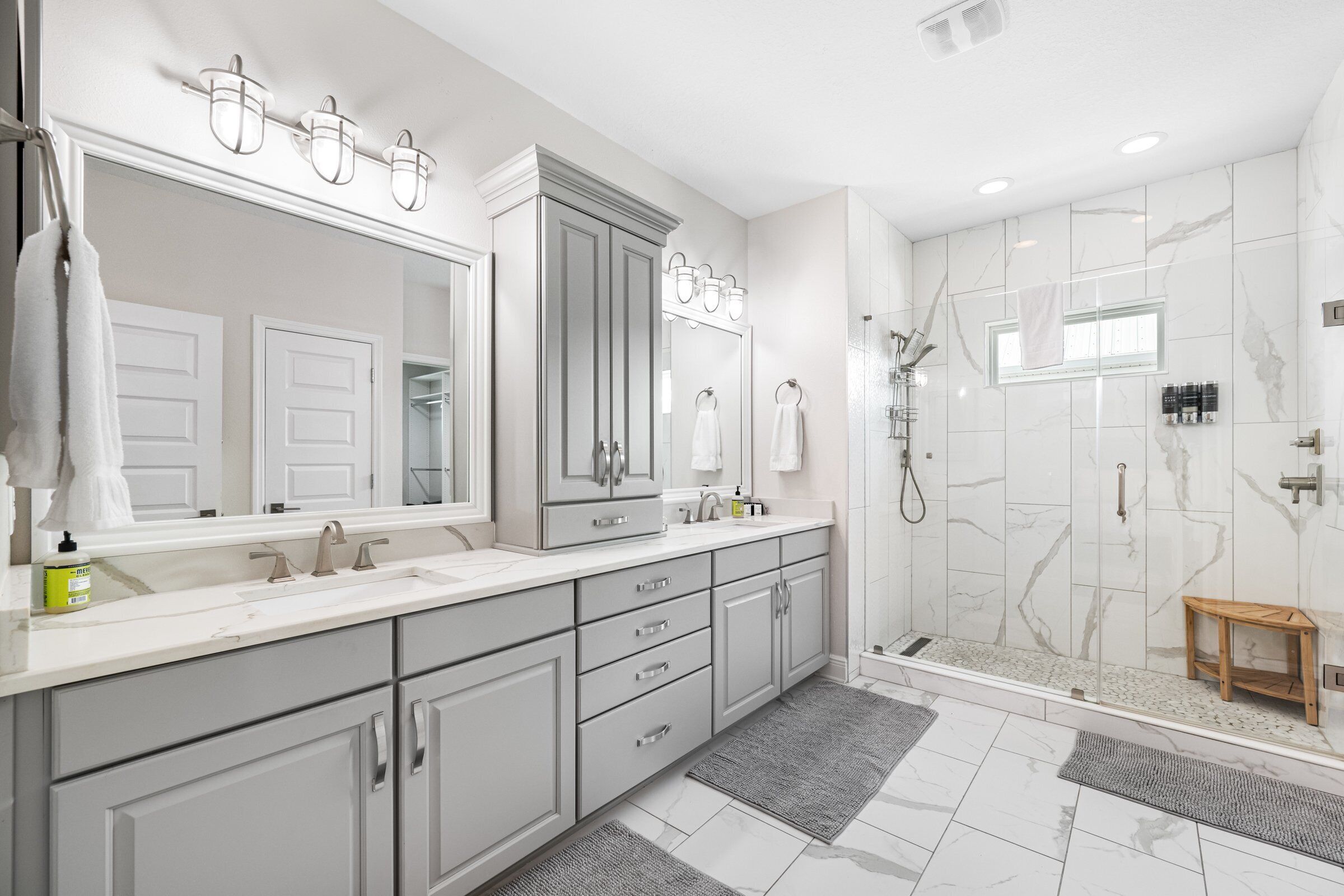 A modern bathroom with two sinks, a large mirror, and a walk-in shower.